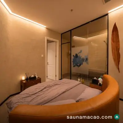 金鳳桑拿 — 圓床房，橙色皮革床圍配灰色床鋪，一面玻璃牆後是淋浴間